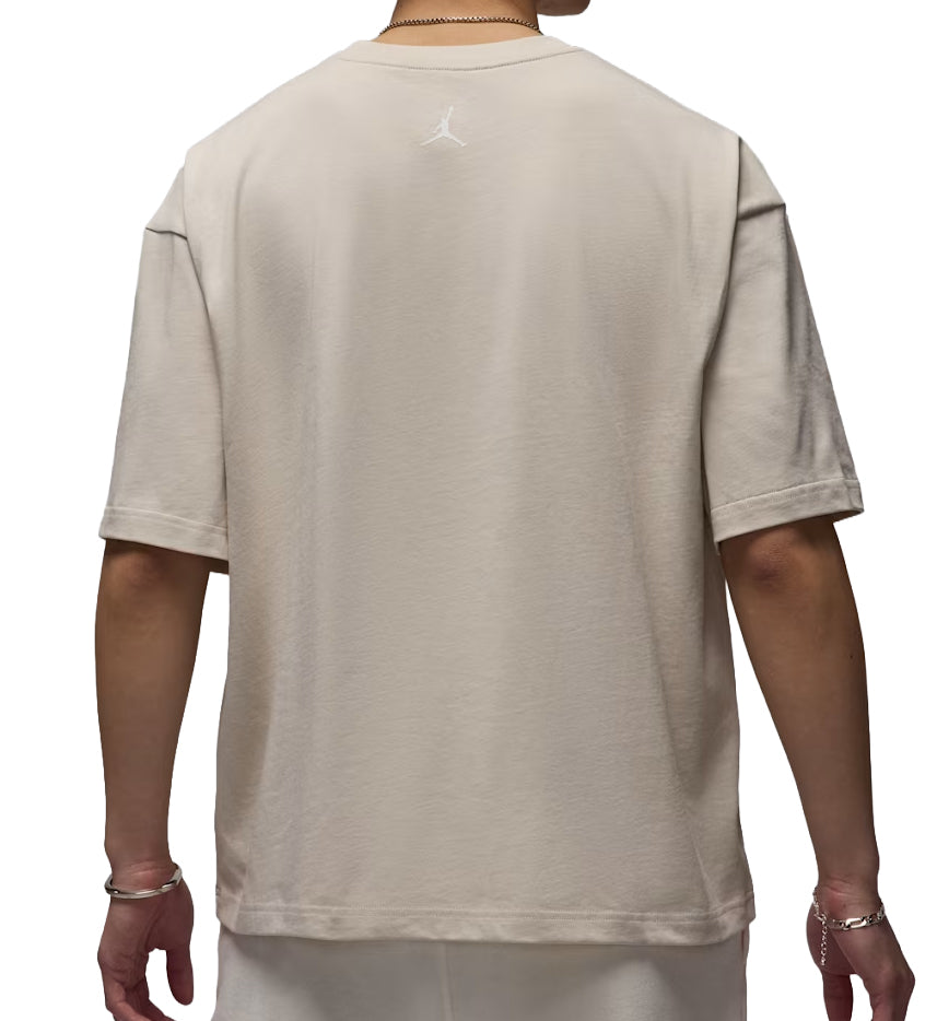 Beige Jordan Flight Essentials t-shirt worn by a person on a white background