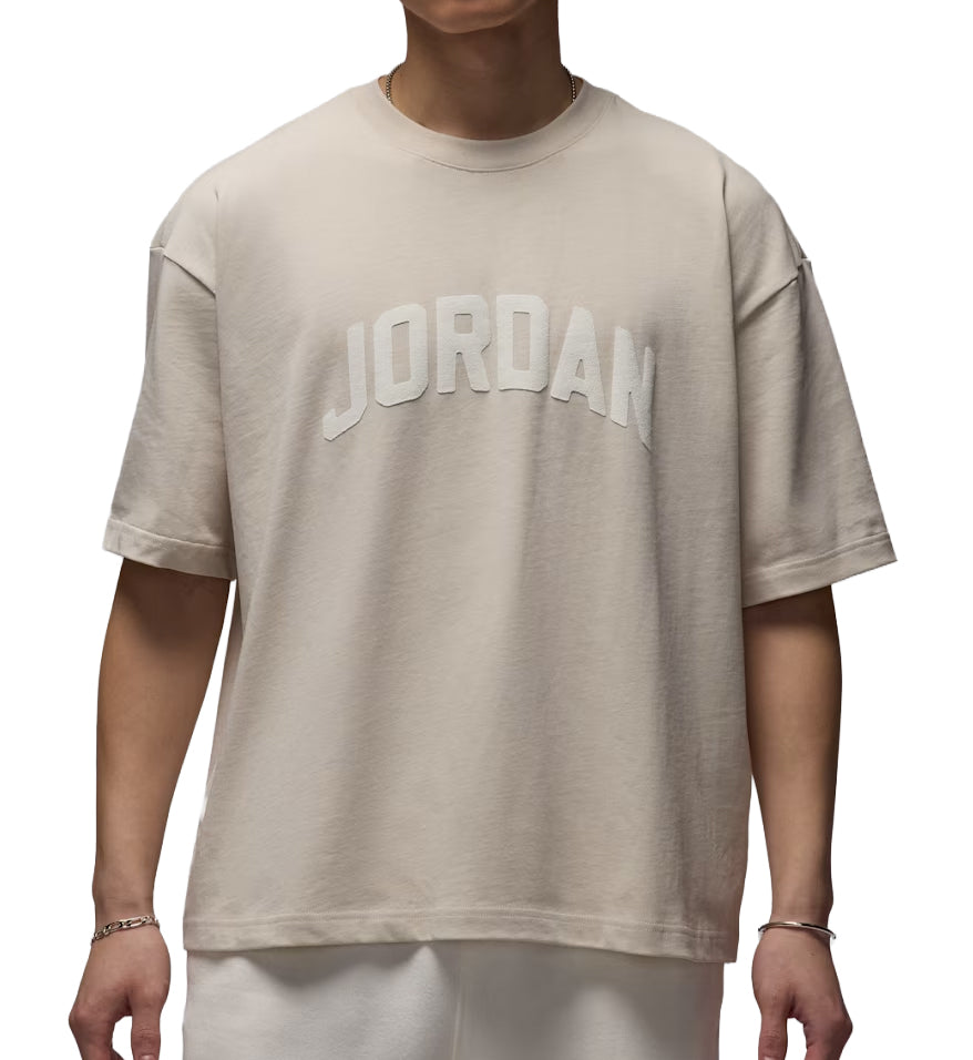 Beige Jordan Flight Essentials t-shirt with 'JORDAN' logo worn by a person on a white background