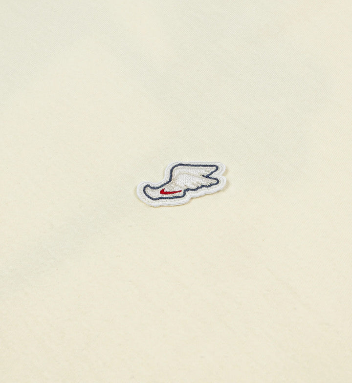 Small embroidered patch of a winged shoe on a beige Nike Max90 T-shirt background
