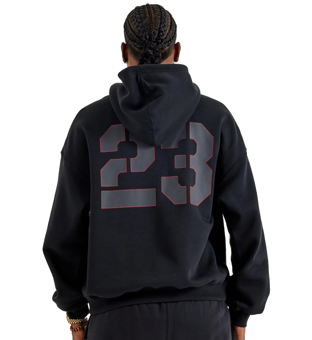 Person wearing a black Jordan Brooklyn Oversized Pullover Fleece hoodie with '23' printed on the back against a white background