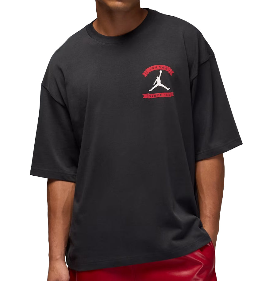Person wearing a black Jordan Oversized Reissue t-shirt with a logo on a white background